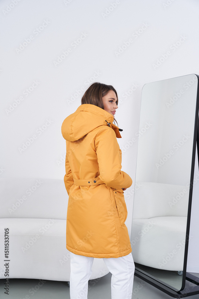 Fototapeta premium Woman wearing yellow coat and boots standing in modern indoor space with mirror