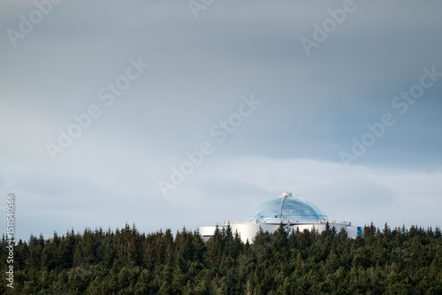 Perlan museum emerging from icelandic forest under cloudy sky photo