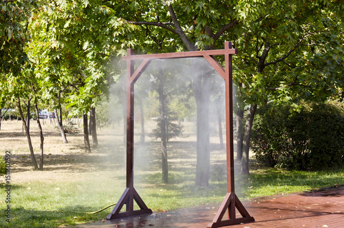 Water spray frame for cooling in hot weather on city street in Kyiv, Ukraine. Water mist cooling fog system in city park on hot summer. Protection against overheating and sunstroke by splashin