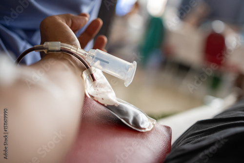 Close-up of a donor's arm with blood flowing through a tube into a blood bag during a blood donation procedure in a medical or clinical setting.