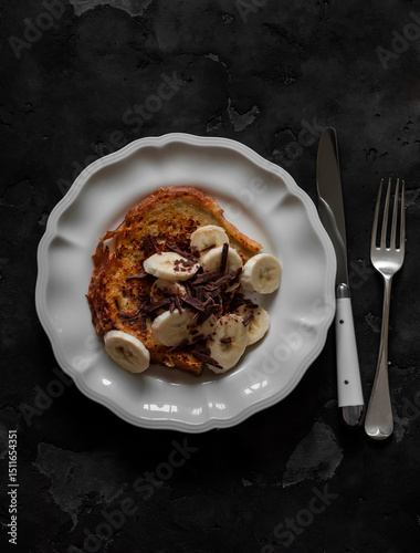 French toast with banana and chocolate chips - delicious breakfast, dessert, snack on a dark background, top view