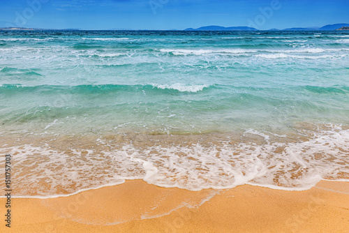 Fototapeta Naklejka Na Ścianę i Meble -  Gentle waves lapping at golden sand on a sun drenched beach, showcasing turquoise waters beneath a clear blue sky