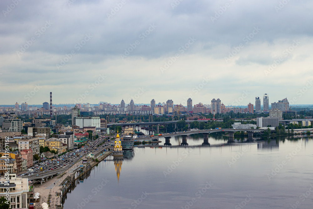 Obraz premium Panoramic view from the Glass Bridge overlooking the Church on the Water, boats on the Dnieper River, and the historic Podil district in Kyiv, Ukraine.