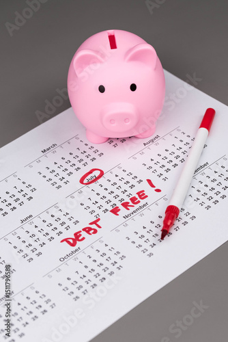 Fototapeta Naklejka Na Ścianę i Meble -  Piggy bank on calendar with the words 'Debt Free' written on it, symbolizing saving money, financial freedom, and achieving a debt-free lifestyle. Concept of financial independence and budgeting.