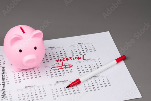 Fototapeta Naklejka Na Ścianę i Meble -  Piggy bank on calendar with the words 'Vacation' written on it, symbolizing saving money for travel, financial planning, and budgeting for a dream getaway. Concept of vacation savings and planning.