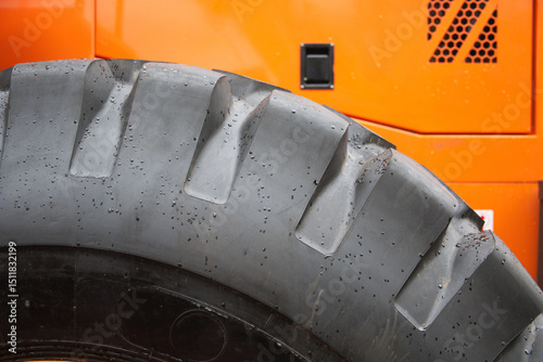 Detailed view of a rugged tire from heavy machinery, showcasing its tread design against an orange backdrop.