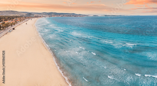 Fototapeta Naklejka Na Ścianę i Meble -  Stunning coastline with houses, hotels, and crystal clear turquoise water meeting sandy beach under a vibrant sunset sky