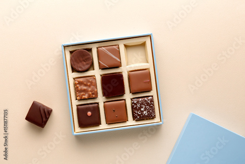 Minimal flatlay of open box with chocolate squares on beige background, elegant candy dessert packaging mockup concept