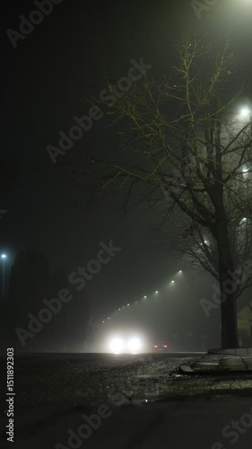 A foggy suburban street with light reflections and cars driving through the mist