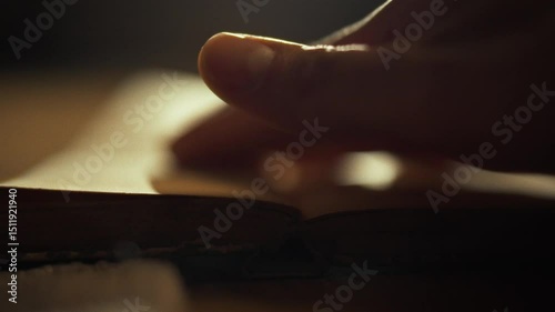 A hand delicately turns the pages of a book, illuminated by soft, warm light. The setting suggests a cozy atmosphere, perhaps in a study or library, evoking a sense of tranquility and focus