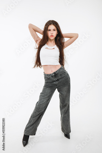 A brunette girl in a white top and gray jeans on a white background.