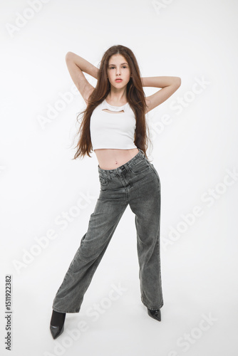 A brunette girl in a white top and gray jeans on a white background.