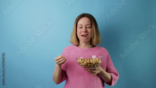 Woman enjoying caramel popcorn snack, cheerful expression, blue background