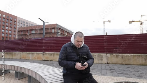 Man using smartphone outdoors in city, smiling while holding a digital device, messaging friends with a smart gadget.