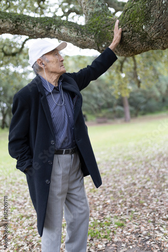 Senior professor enjoying retirement walking in park touching tree branch