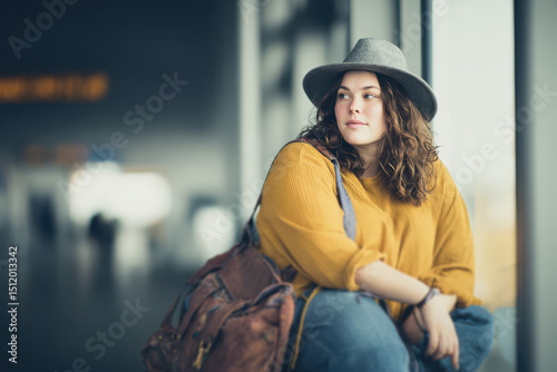 Modern plus size woman sitting confidently at airport gate with luggage waiting for her flight