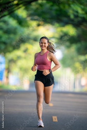 A woman is running on a road. She is wearing a pink shirt and black shorts. The road is paved and has a few trees in the background