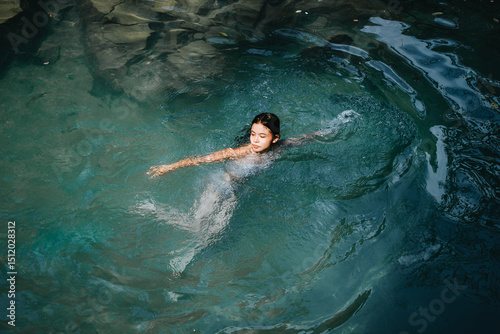 A woman is swimming in a pool. The water is blue. The woman is wearing a white bathing suit