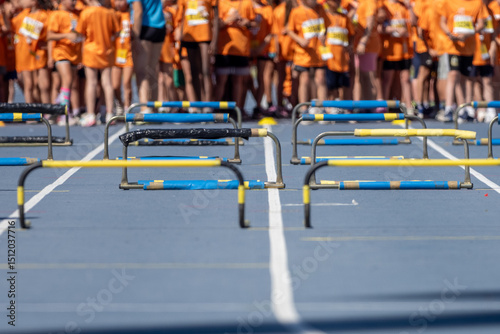 Wallpaper Mural Blue athletics track with yellow and black hurdles aligned and young athletes waiting in the background Torontodigital.ca