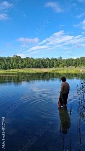 Tranquil lake scene with clear blue water, green reeds, and a lush forest under a bright sky. Perfect nature landscape for relaxation, travel, or outdoor themes.