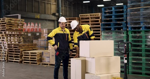 Two multicultural male warehouse workers inspecting cardboard boxes for shipping while checking list and discussing content in active motion scene inside organized cargo facility