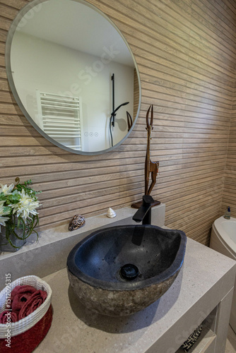 Un meuble vasque de salle de bains moderne noir avec derrière un mur en imitation carrelage bois et un grand miroir