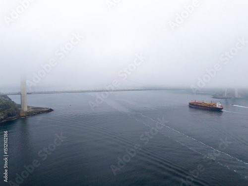 Misty harbor view with cargo ship and harbor structures. An aerial, full-shot view of a harbor shrouded in a light mist. Yavuz Sultan Selim Bridge Istanbul Turkey Turkiye Beykoz Poyrazkoy Anatolian  photo