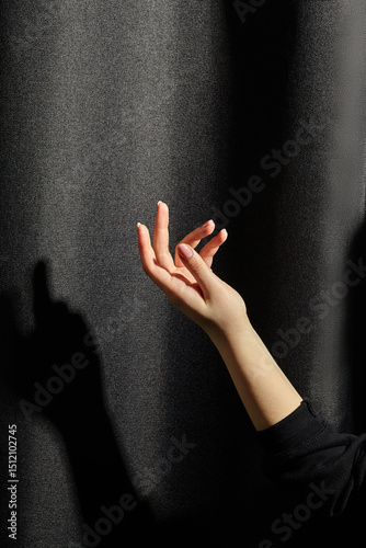 Woman hand reaching for light against dark background with shadow