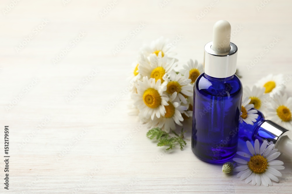 Bottles of essential oil and chamomile flowers on light wooden table, closeup. Space for text Bottles of essential oil and chamomile flowers on light wooden table, closeup. Space for text