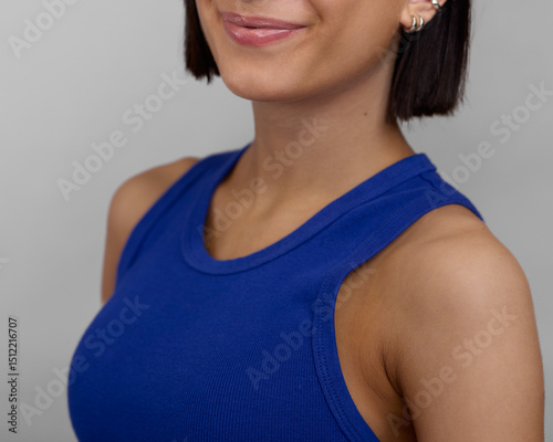 Close-up of a young woman smiling softly, wearing a royal blue tank top. The image highlights smooth skin, minimal makeup, and silver hoop earrings, creating a clean, modern, and confident vibe ideal 