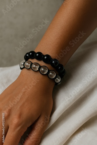 Close-up of a hand wearing black and clear beaded bracelets on beige fabric