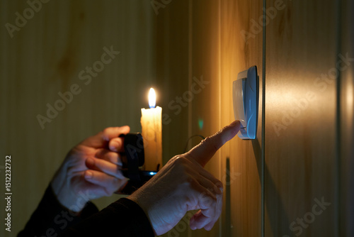 Photography A man with a burning candle in his hand turns a light switch on and off