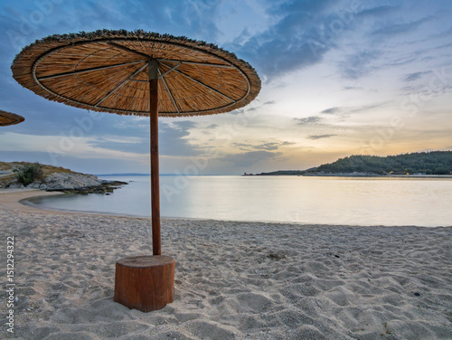 Fototapeta Naklejka Na Ścianę i Meble -  Serene beach with straw umbrellas at sunset in Toroni on Sithonia peninsula, Greece