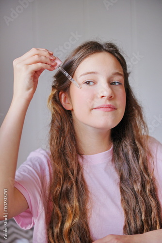 Cute girl applying skincare product with a dropper while smiling, showcasing a focus on self-care at home during the day
