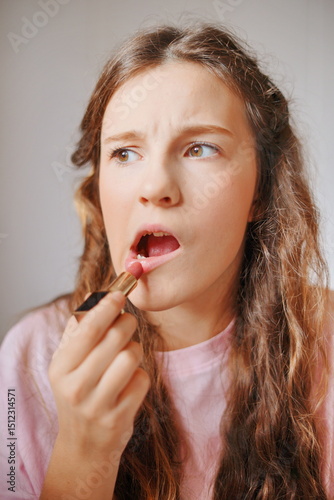 Girl applying lipstick while contemplating her look, showcasing her adorable features and playful expression in a bright indoor setting