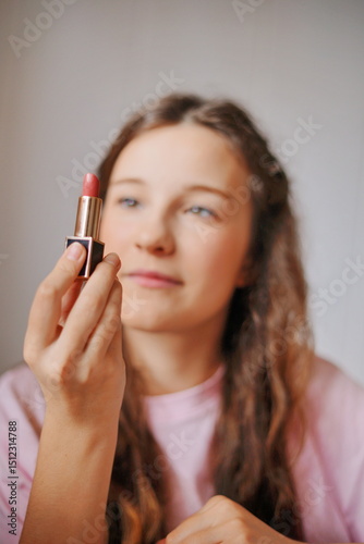 Adorable girl examines a lipstick tube with curiosity while sitting indoors in soft light during the daytime