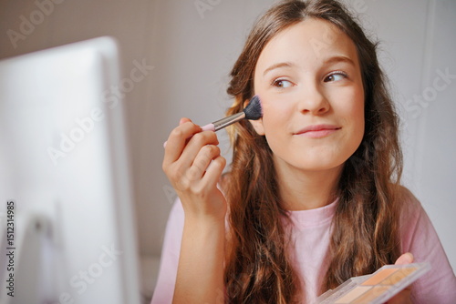 Girl applying blush while looking in the mirror at home, bright natural light highlighting her adorable features and creativity