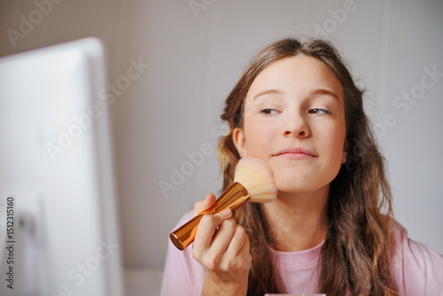 Adorable girl applying makeup with a brush in a bright, modern room while preparing for a special occasion