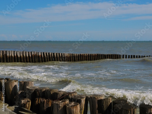 Fototapeta Naklejka Na Ścianę i Meble -  Lido di Volano, in the province of Ferrara, Northern Italy. Sea and waves, with a barrier of wooden poles to combat coastal erosion.