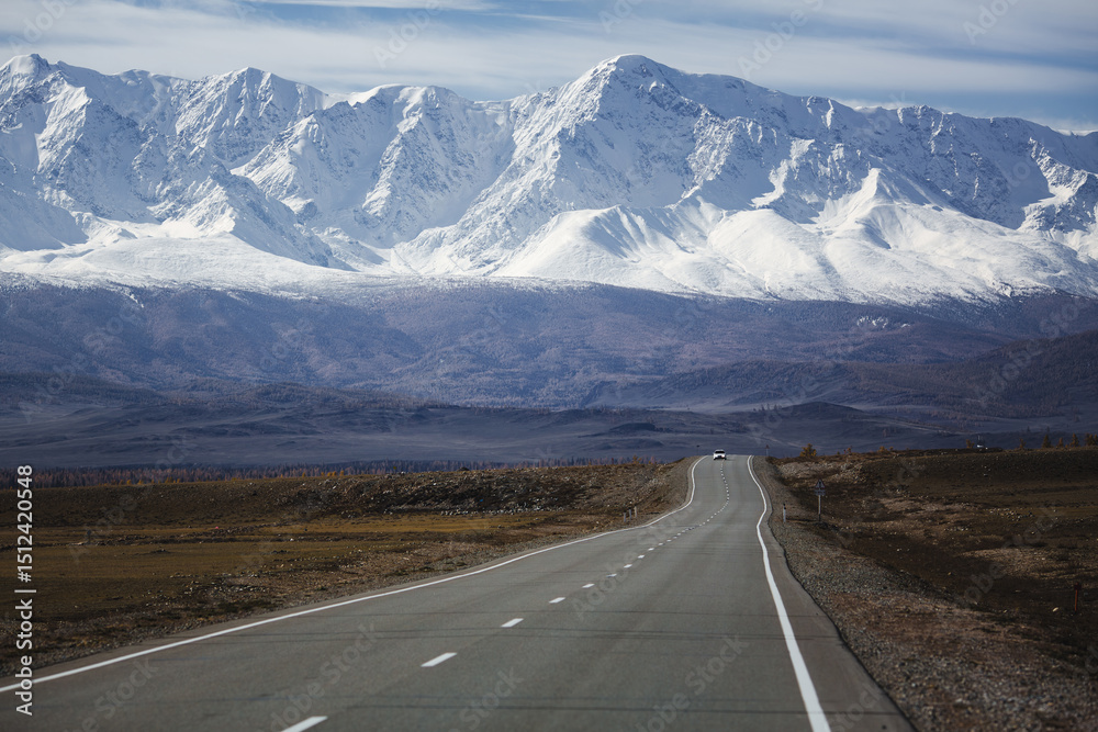 Fototapeta premium A lonely road stretches into the North Chuya Range in the Altai Republic, disappearing toward massive snowfields that blanket the towering peaks. The landscape is vast, cold, and majestic.