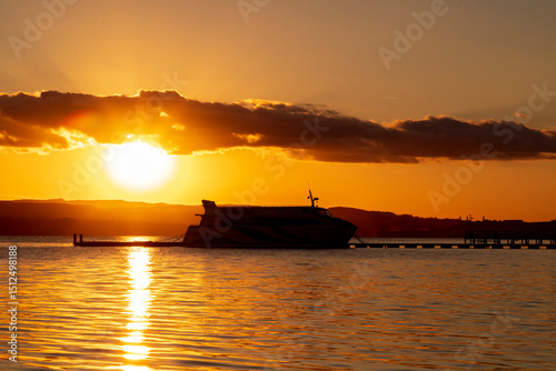 A ferry silhouetted against a vibrant sunset over calm water.