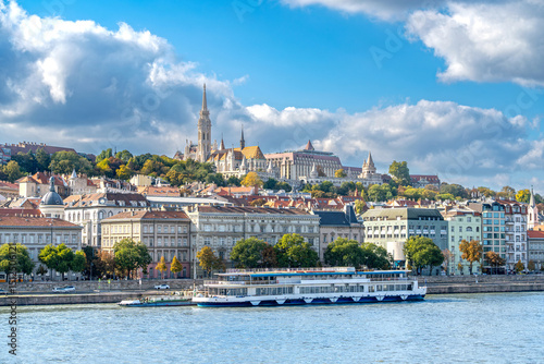 Majestic Buda Castle Hill Panorama with River Cruise Ship on Danube - Historic Budapest Skyline featuring Matthias Church Spires and Autumn Foliage Against Dramatic Clouds