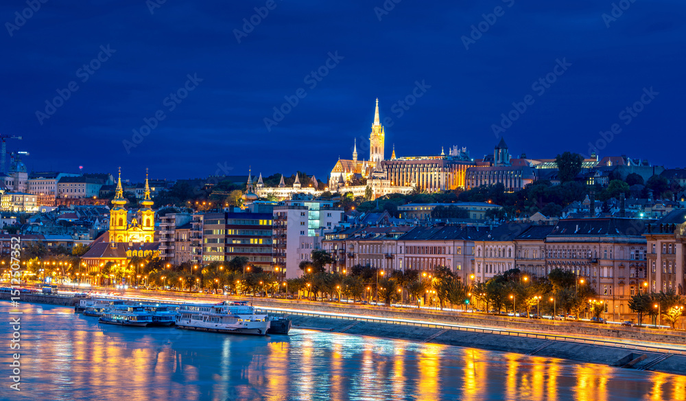 Obraz premium Matthias Church in Fisherman's Bastion illuminated at night, with the Danube River reflecting the glowing lights of Budapest, Hungary