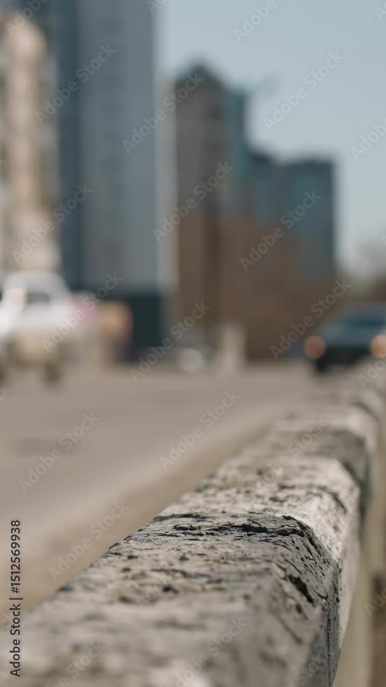 Close view of a city road with cars in motion in the background, the focus is on the weathered road barrier and cars in motion