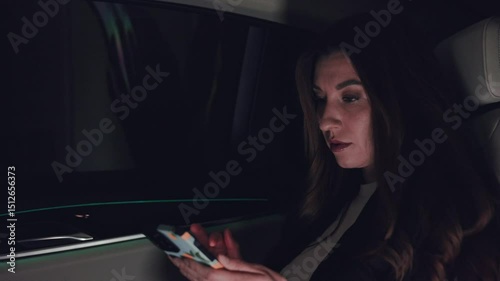 business woman in back seat of car at night using smartphone, driving home after work