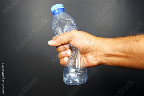 hand holding a used water bottle crushing by hand on dark background closeup view 
