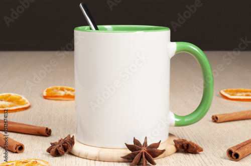 Blank two-tone 11oz mug on on the table. Mug with warm spices like cinnamon, star anise, dried orange. Green handle. Mug mockup