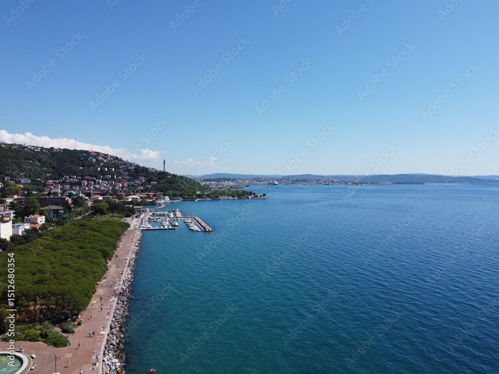 Fototapeta premium A stunning drone view of Trieste from Barcola, showcasing the city's coastline, historic buildings, and Adriatic charm under a clear northern Italian sky.