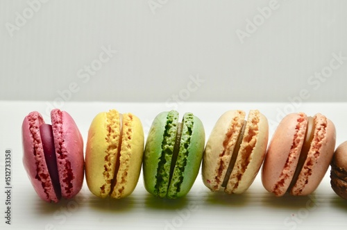Row of five macarons stood on edge on a white marble background.