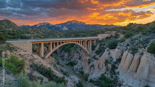 Dramatic sunset over a bridge spanning a canyon.  A majestic arching bridge crosses a river valley, framed by dramatic, colorful clouds and mountains